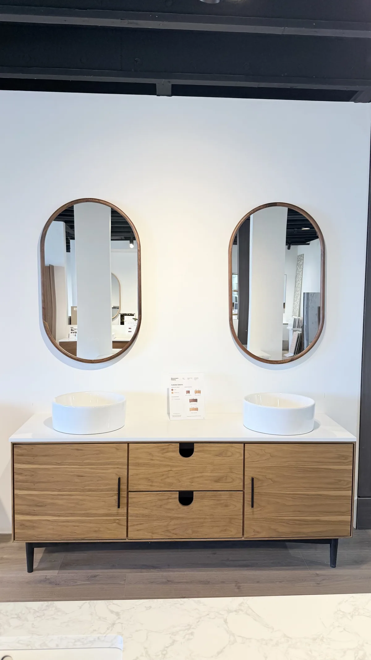A double-basin oak vanity with two oval mirrors on the showroom floor