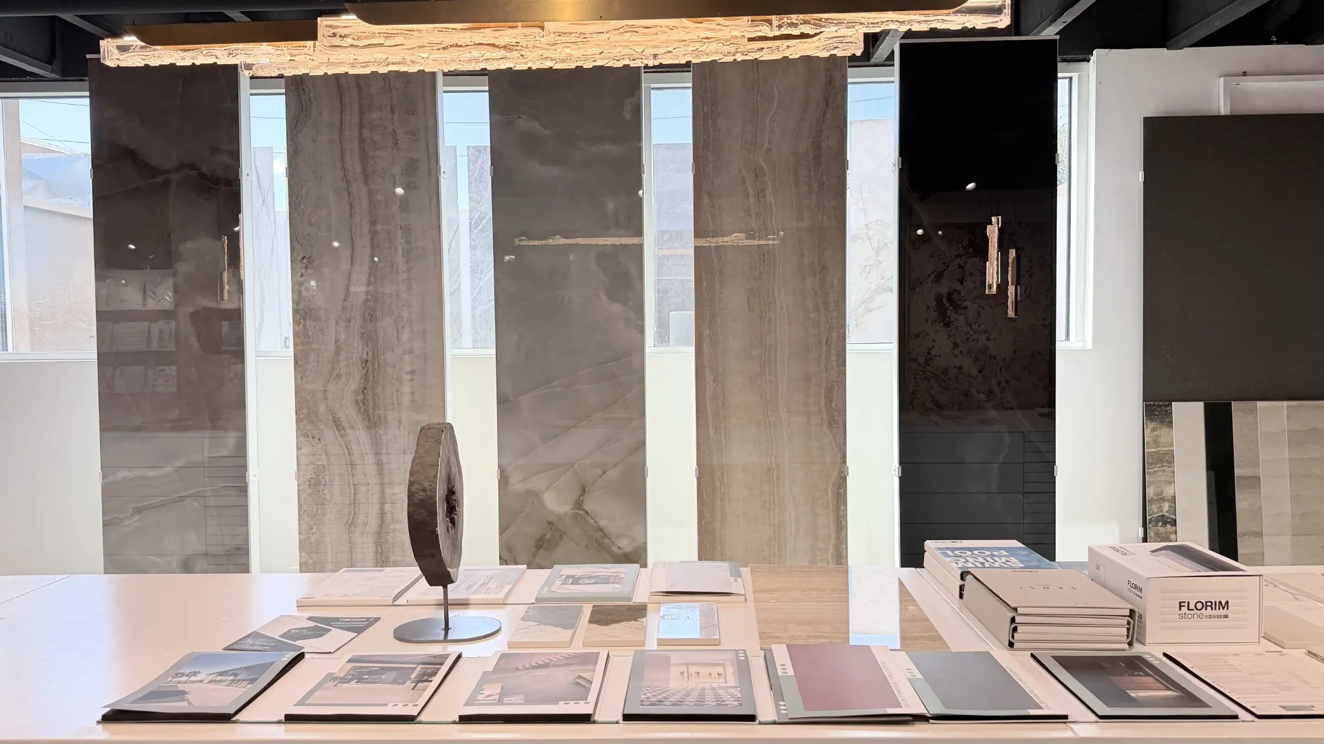 Full-height stone slabs standing against the windows of the Segna Tile showroom, with material boards laid out on the table in front